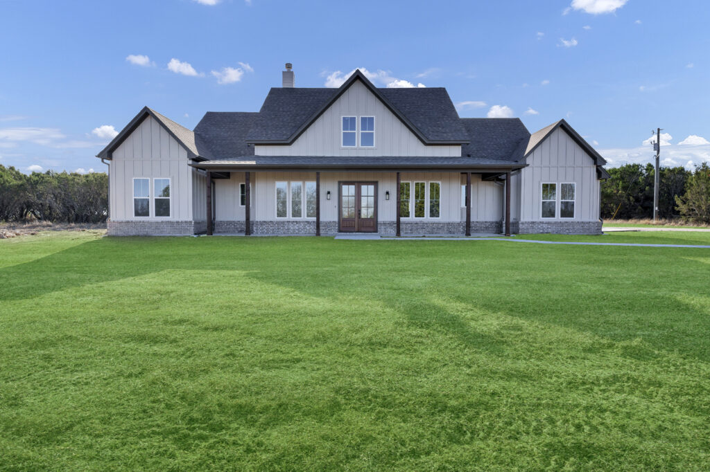 Custom white modern farmhouse by True Texas Builders with black roof and large front lawn in Texas